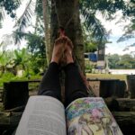 best travel books to read in the photo author is lying down with book on her lap in malaysia kinabatagan river homestay