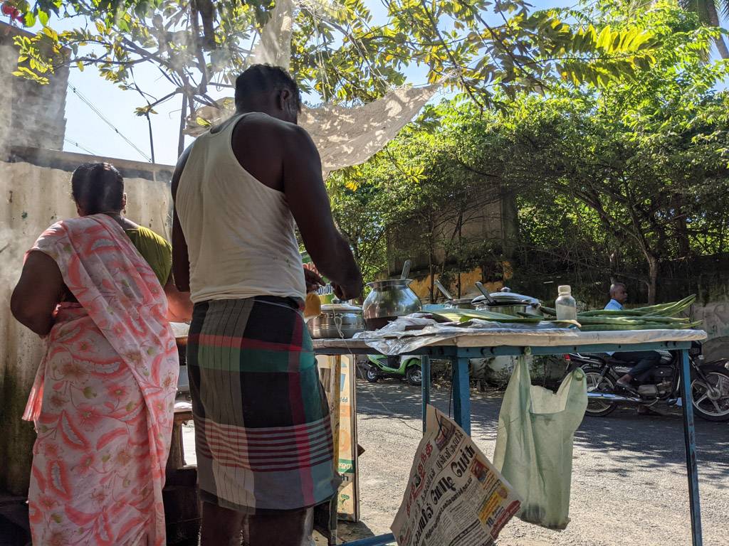 a couple busy providing breakfast early morning on the street. notice the drumsticks on the table. must be from their backyard and more than what they need and hence to be sold.