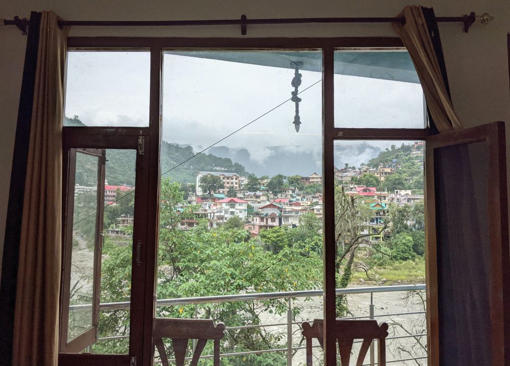 a window worth having. view of homes with slant roofs, mountains, river beyond a window and balcony