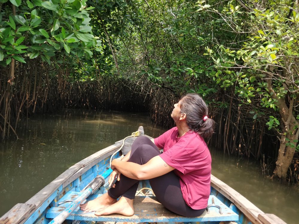 the author sitting on a boat going inside the green mangroves on a muddy river