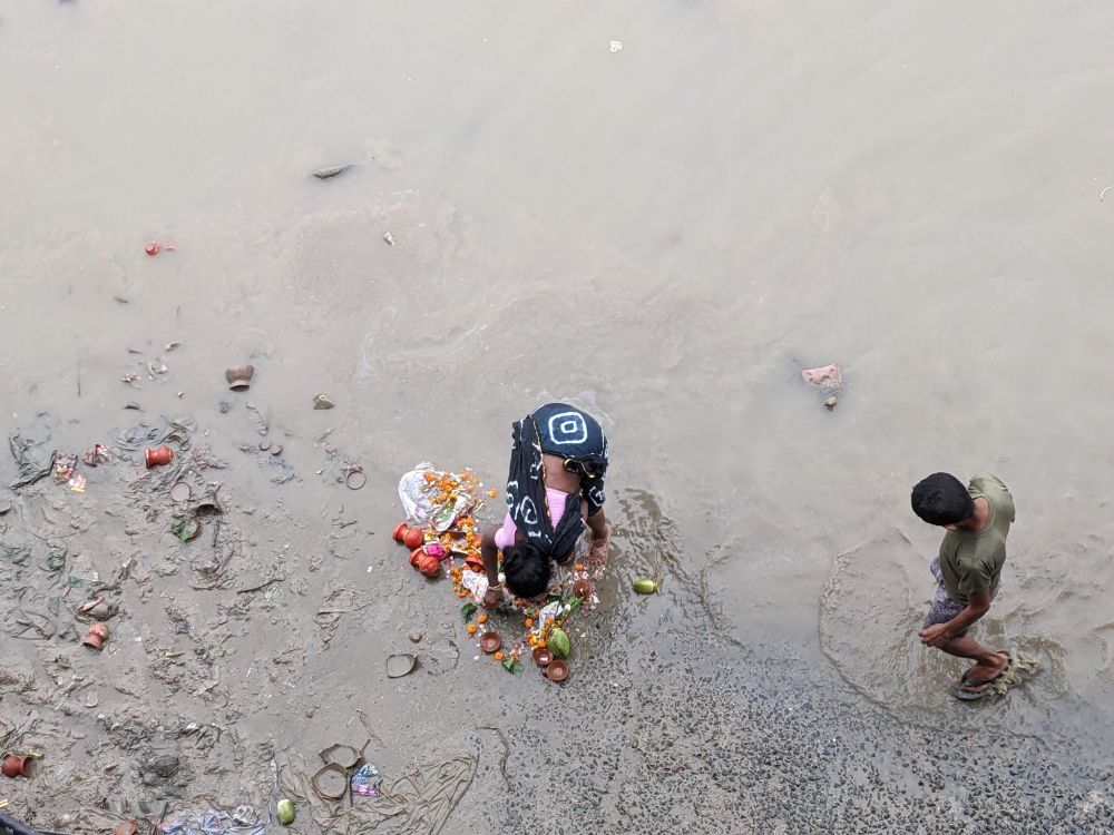 at the bank of ganga, a woman separating things of use from an offering into the river by a devoteee