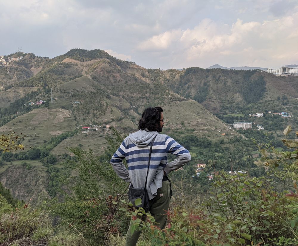 he looks a bit irritated, maybe i dragged him out on a work day. a man standing in a valley with mountains visible all around him