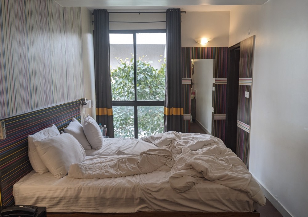 a hotel room with slept-in bed, open window, a mirror, lights on
