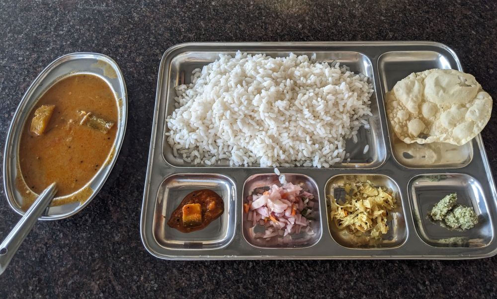 another simple rice thali meal in Muthanga in Kerala. rice, salad, papadum, vegetable. pickle chutney, sambhar on a steel plate