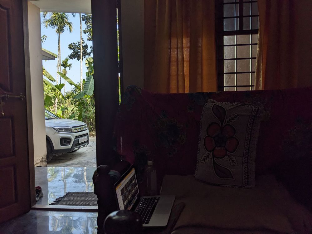 couch turned into a work desk and the view of outside with a car parked and plants