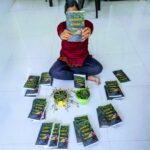 feature a girl holding a book called Journeys beyond and within surrounded by many copies of the book in a home (1)