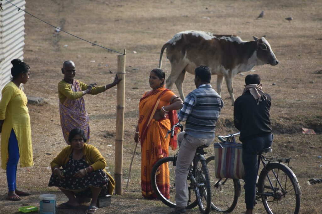 a group of people in traditional saris and regular clothes standing on an open ground and talking