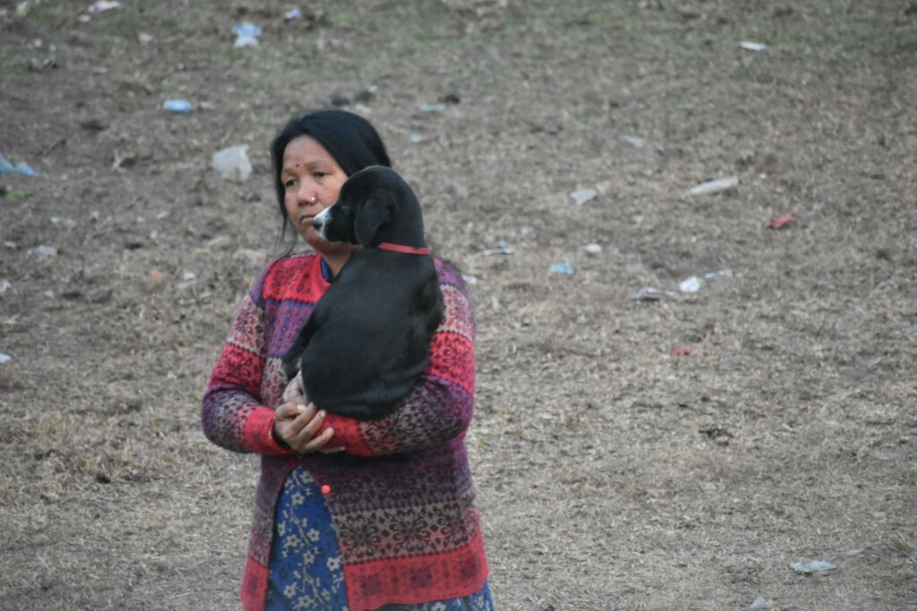 a woman in red sweater looking very sad carrying her black puppy in her arms and walking as if it was a baby