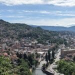 the city of sarajevo with the river red brick buildings mountains used as feature image for best things to do in sarajevo