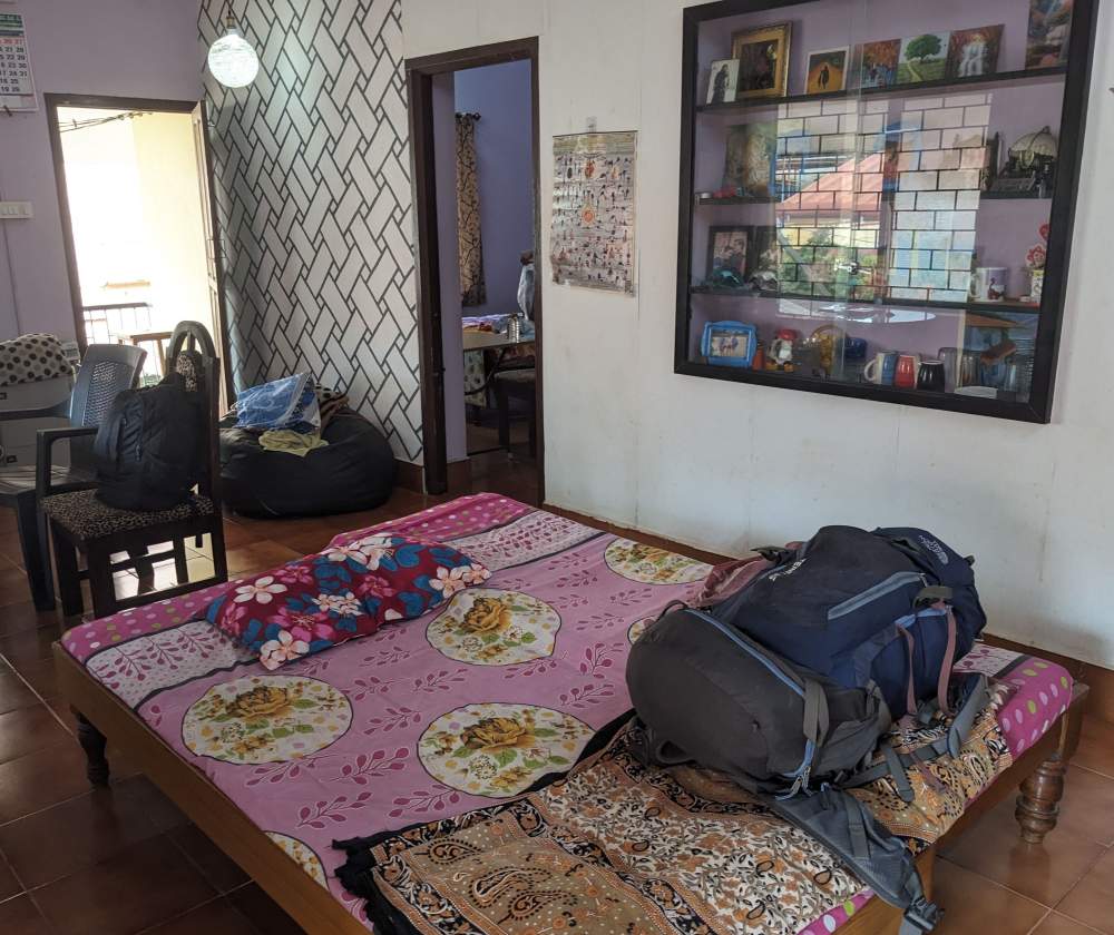 the colorful hall of our home stay in mangalore a room with a bed backpacks a cabinet with decorative items (1)